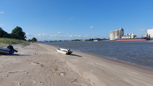 Ein Boot liegt an einem Sandstrand vor einer Industrie-Kulisse.