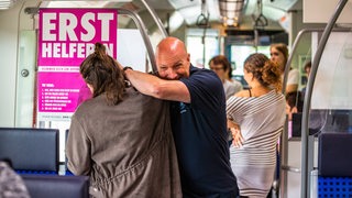 Gestellte Szene eines Angriffs gegen eine Frau durch einen Mann in einer Straßenbahn. Im Hintergrund stehen Fahrgäste. (Symbolbild)