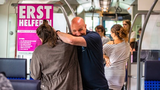 Gestellte Szene eines Angriffs gegen eine Frau durch einen Mann in einer Straßenbahn. Im Hintergrund stehen Fahrgäste. (Symbolbild)