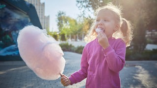 Ein kleines Mädchen mit Zöpfen isst rosa Zuckerwatte.