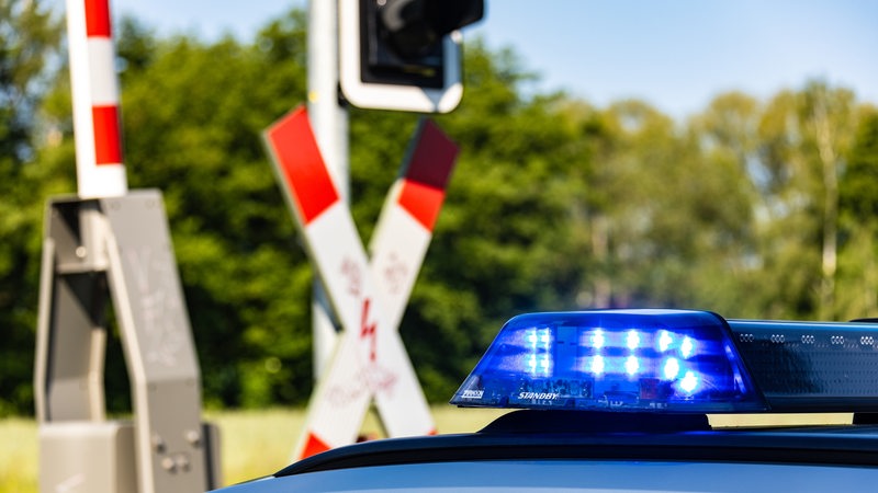 Ein Einsatzfahrzeug der Polizei steht vor einem beschrankten Bahnübergang.